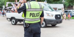 Back view of police officer at public July 4 parade street event near Dallas, Texas, America. Law enforcement and security guard at live festival event.